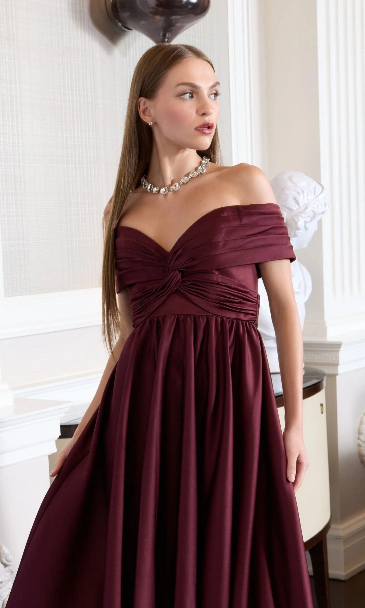 A woman in a Mac Duggal 56188 long formal dress and a pearl necklace stands indoors, gazing thoughtfully to the side.